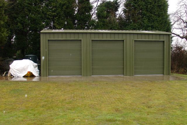 A green builiding with three bays with their roller doors closed