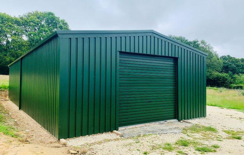 Perspective view of a green steel storage building with a central roller door on a gravel foundation.
